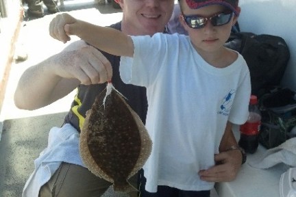 Man and boy on boat, holding a freshly caught flatfish.