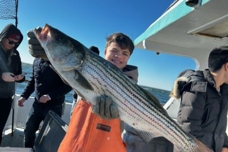 Person in orange overalls holding a large striped fish on a boat.