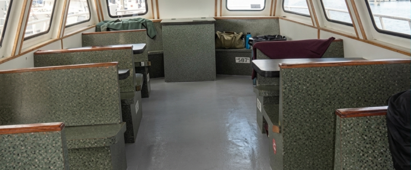 Inside a boat cabin with empty green benches and large windows.