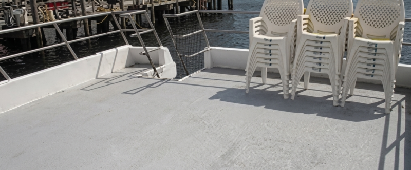 Empty ferry deck with stacked chairs beside a harbor.