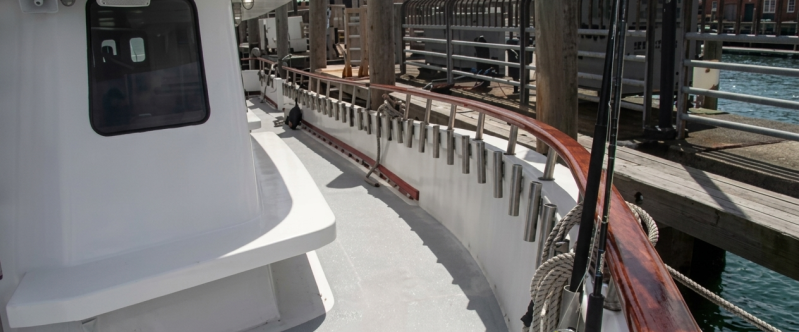 Boat deck with railing and fishing rods docked at a wooden pier.