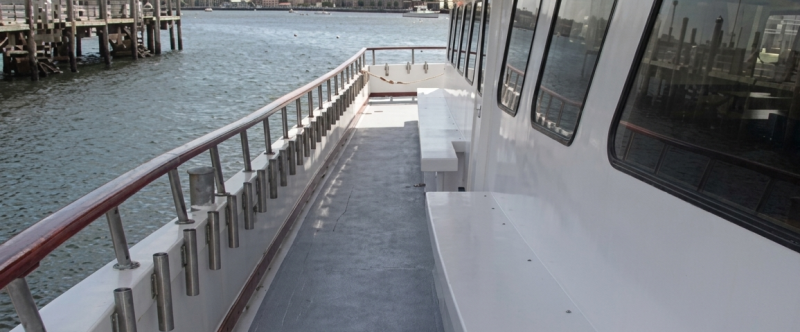 View of a boat's side deck with benches, overlooking a harbor.