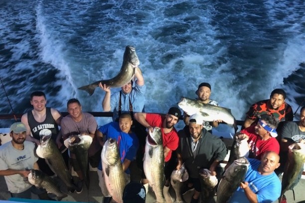 Group of people on a boat holding large fish with ocean waves behind.