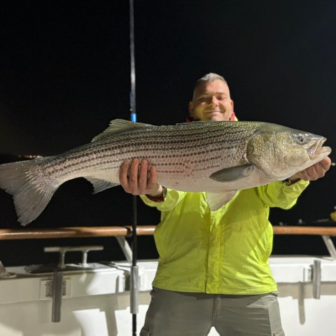 Person on boat holding large fish at night.