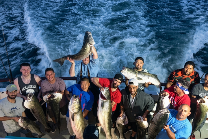 Group of people on a boat holding large fish, ocean waves in the background.
