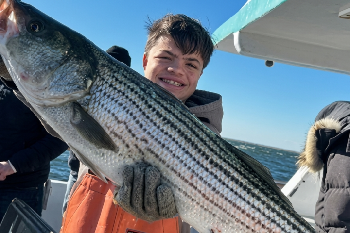 Person holding a large striped bass on a boat with others in jackets.