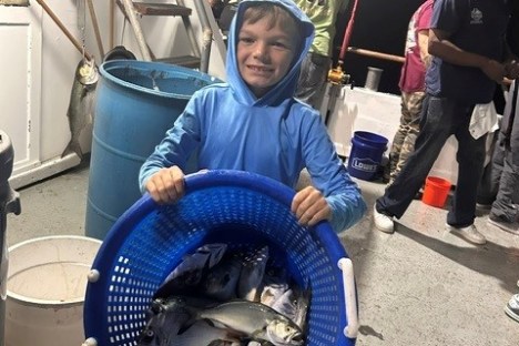 Child holding a blue basket of fish on a boat, with others nearby.