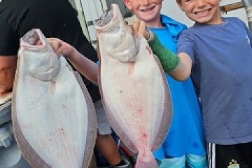 Two smiling boys holding large fish on a boat.