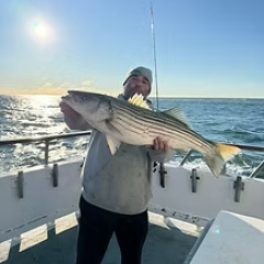 Person holding a large fish on a boat with ocean backdrop.
