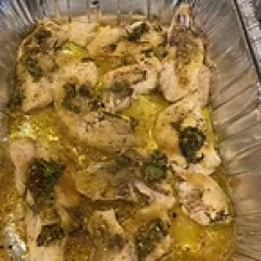 Cooked chicken wings in oil with herbs in a tray.