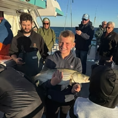 Boy smiling holding a fish on a boat with people in the background.