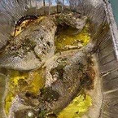 Two cooked fish with herbs and oil in a metal tray.