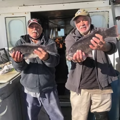 Two men on a boat holding fish and wearing caps and jackets.