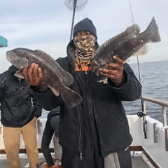 Person on boat holding two fish, wearing black jacket and camo mask.