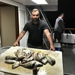 Man holding a tray of fish on a boat deck.