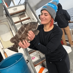 Person on a boat holding a fish, wearing a beanie and black clothing.