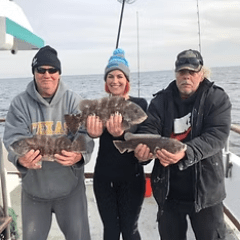 Three people on a boat holding fish, wearing winter clothing.