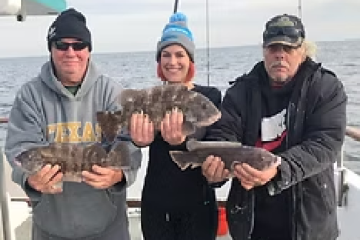 Three people on a boat holding fish, wearing winter clothing.