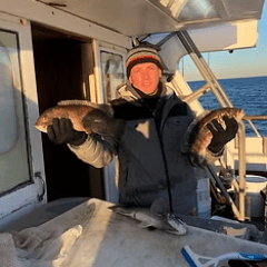 Person on boat holding two fish, another fish on table.