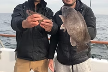 Two men on a boat holding fish, wearing jackets and caps.