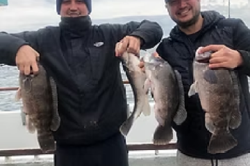 Two men holding large fish on a boat, smiling at the camera.