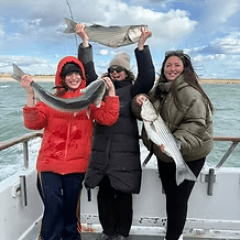 Three people on a boat holding fish, smiling, with cloudy sky.