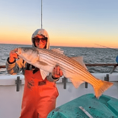 Person holding a large fish on a boat at sunset.