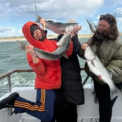 Three people on a boat holding large fish and smiling.