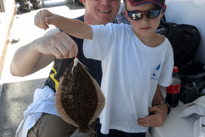Child holding a flatfish on a boat, assisted by an adult.