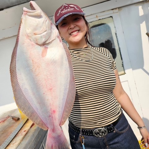 Person in striped shirt holds large flat fish on a boat.