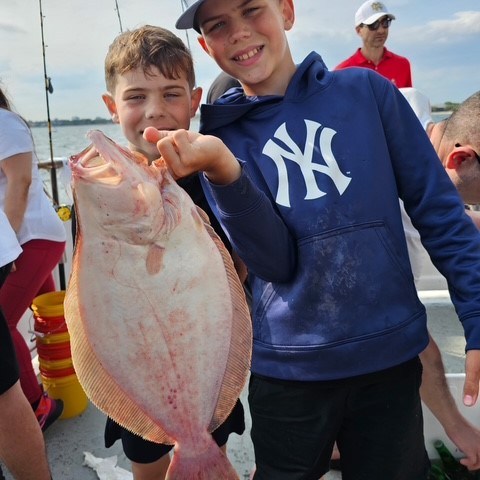 Two boys on a boat holding a large fish, smiling at the camera.