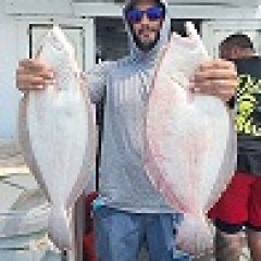 Person holding two large fish on a boat, wearing a hooded shirt and sunglasses.