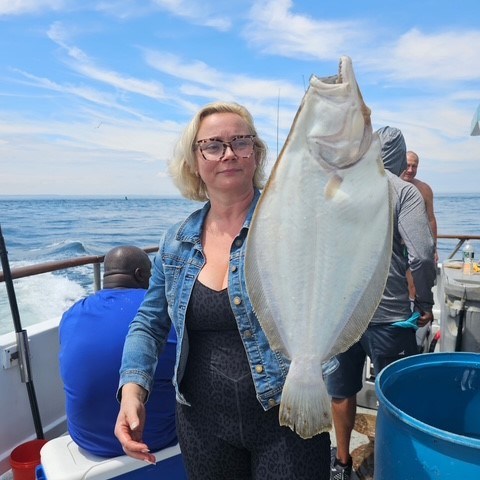 Woman on boat holding a large fish with ocean background.