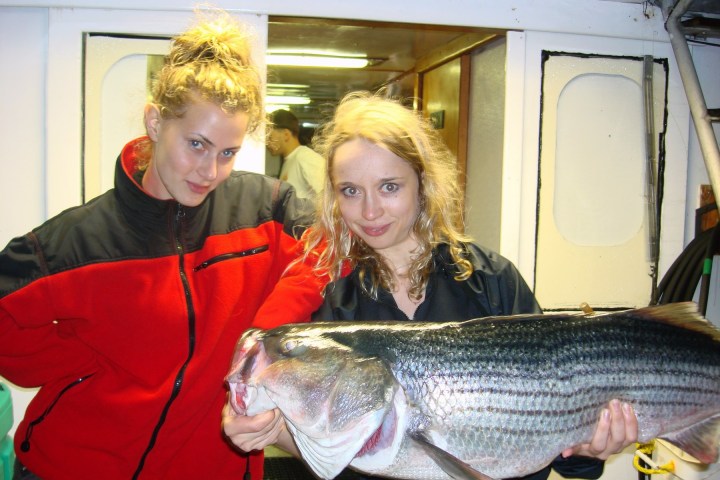 Two women holding a large fish on a boat.